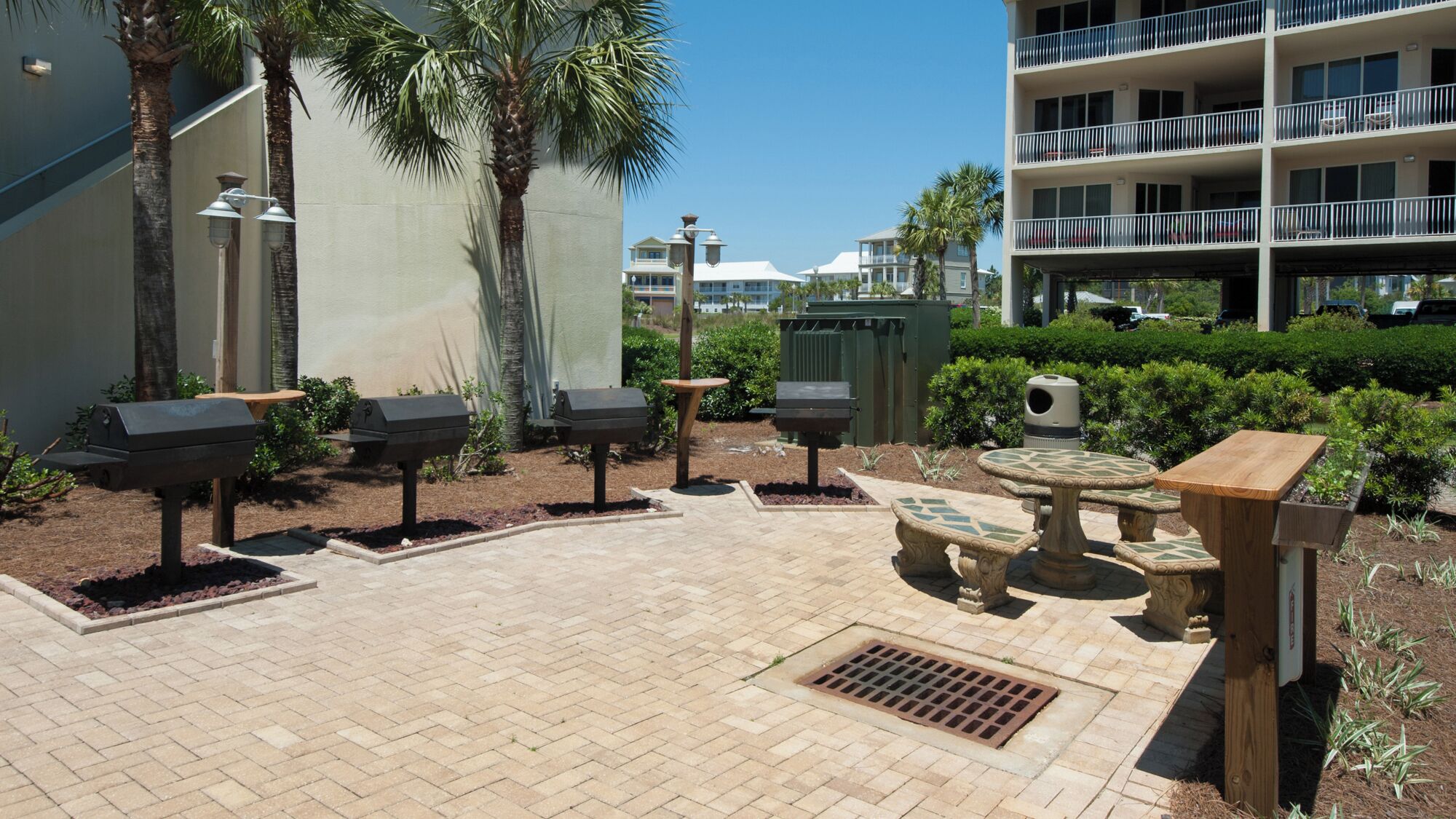 Un espace extérieur aménagé en terrasse, avec un sol en briques, des barbecues et une table ronde entourée de chaises.