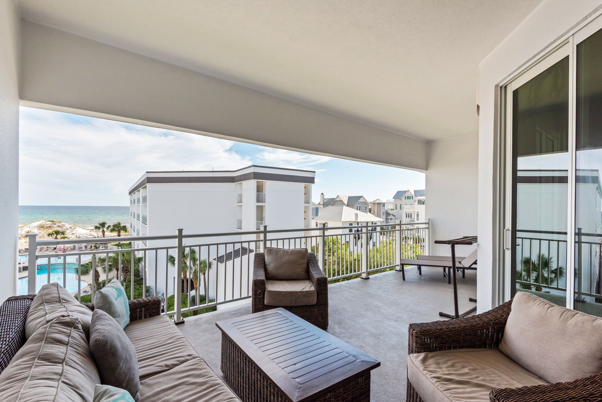 Un balcón con mobiliario exterior, una piscina y vistas a edificios y al mar.