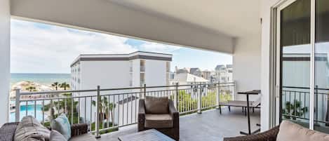 Un balcón con mobiliario exterior, una piscina y vistas a edificios y al mar.