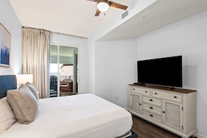 Une chambre d’hôtel avec un lit, un téléviseur posé sur une commode, un ventilateur de plafond et une vue sur la mer par la fenêtre.