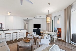 Ein modernes Wohnzimmer mit Essbereich, einer Küche und einem großen Fenster mit Vorhängen.