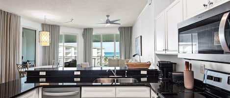 A modern kitchen with a black countertop, white cabinets, a stainless steel microwave, and a ceiling fan.