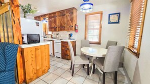 A compact kitchen with wooden cabinets, a microwave, a stove, and a dining table with chairs. - Paradise  Gruene Cottages (New Braunfels)