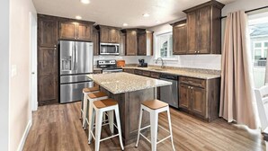 A modern kitchen with dark wood cabinets, stainless steel appliances, a granite countertop island, and bar stools. - Red Bridge Retreat | Gym | Ping-Pong | Near Golf (Eagle Mountain)