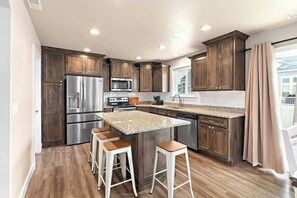 A modern kitchen with dark wood cabinets, stainless steel appliances, a granite countertop island, and bar stools. - Red Bridge Retreat | Gym | Ping-Pong | Near Golf (Eagle Mountain)