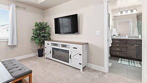 A modern living room with a flat-screen TV, a potted plant, a fireplace, and a view into the adjacent bathroom. - Red Bridge Retreat | Gym | Ping-Pong | Near Golf (Eagle Mountain)