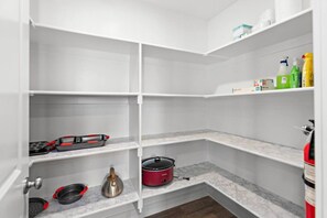 A kitchen with white cabinets, a marble countertop, and various kitchen appliances including a red slow cooker and a kettle.