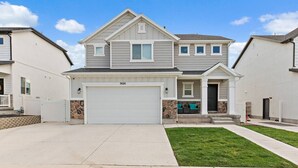 A two-story house with a garage, a stone accent wall, and a well-maintained lawn. - Red Bridge Retreat | Gym | Ping-Pong | Near Golf (Eagle Mountain)