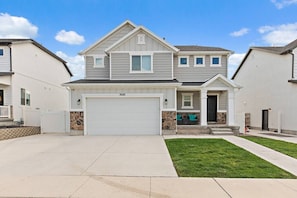 A two-story house with a garage, a stone accent wall, and a well-maintained lawn. - Red Bridge Retreat | Gym | Ping-Pong | Near Golf (Eagle Mountain)