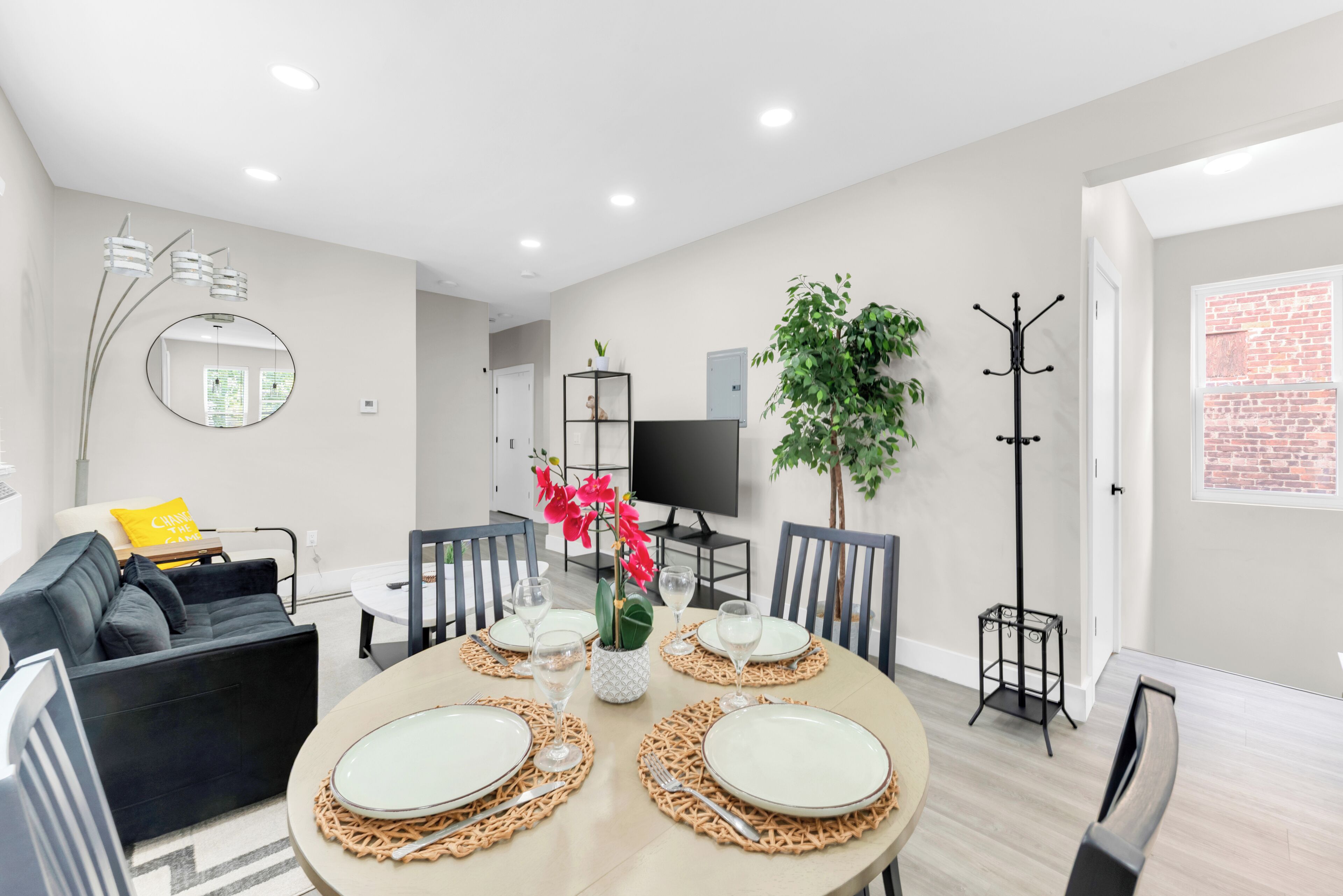 A modern living room with a round dining table set for four, a sofa, a TV, and a coat rack.