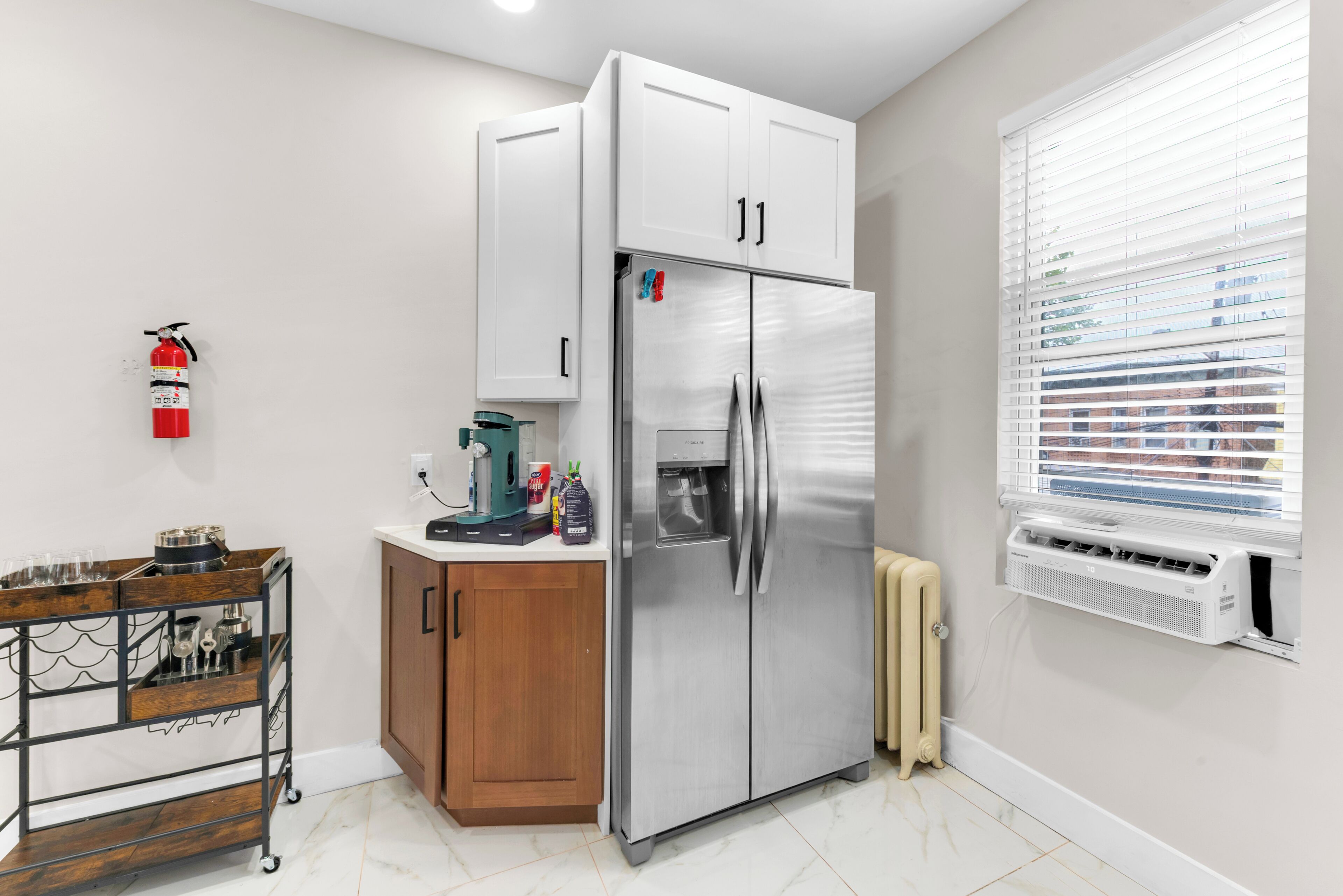 A compact kitchen with a stainless steel refrigerator, a coffee machine, and a small cabinet.