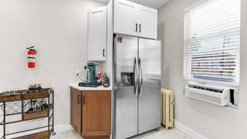 A compact kitchen with a stainless steel refrigerator, a coffee machine, and a small cabinet.