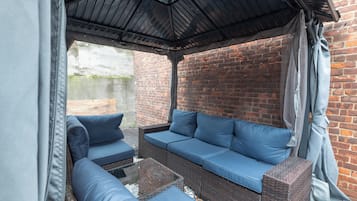 A covered outdoor seating area with a brick wall backdrop.