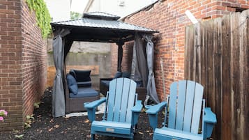 A backyard with a brick wall, a wooden fence, a gazebo, and two Adirondack chairs.