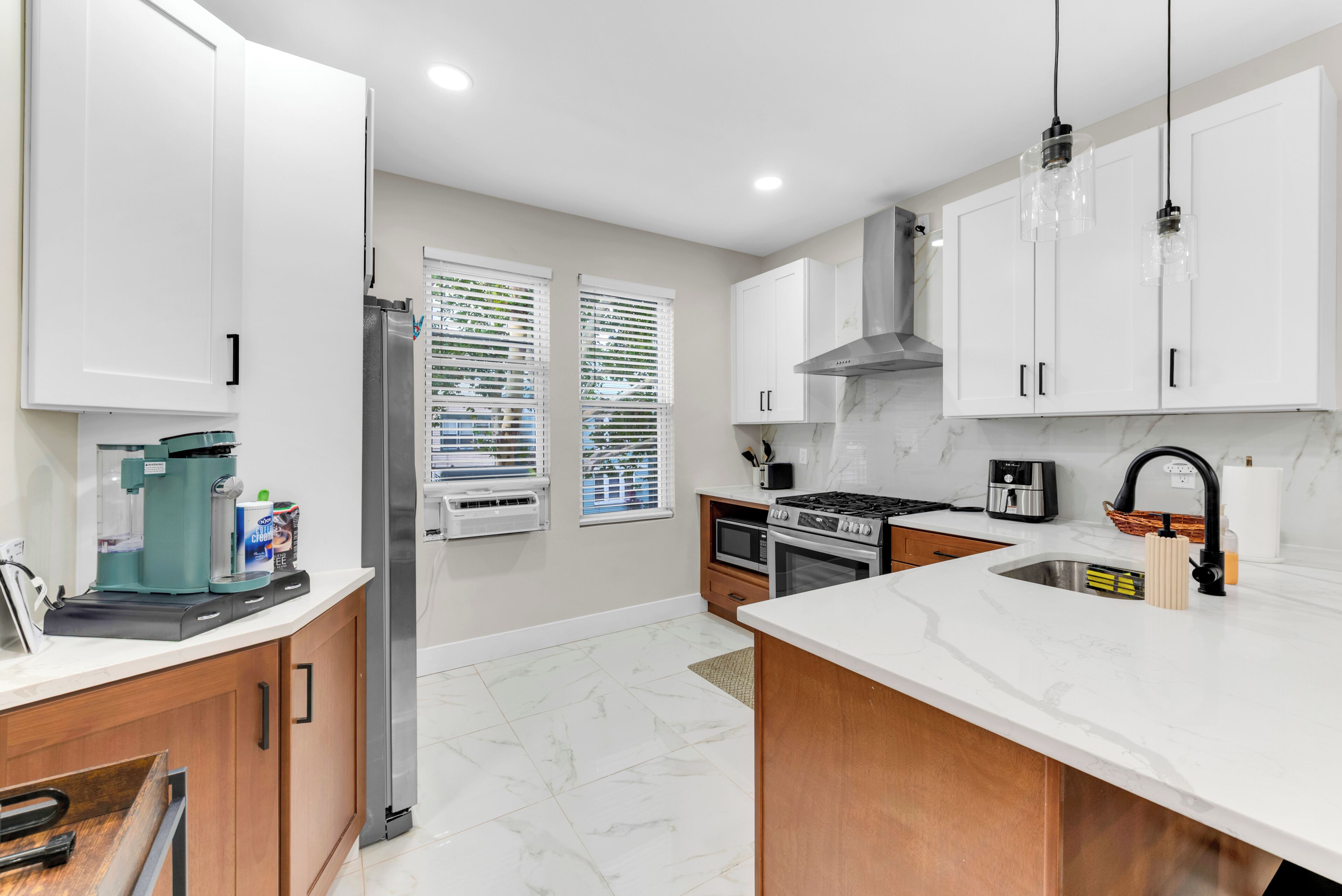 A modern kitchen with white cabinets, a stainless steel refrigerator, a built-in oven, and a coffee maker.