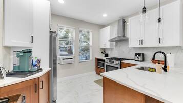 A modern kitchen with white cabinets, a stainless steel refrigerator, a built-in oven, and a coffee maker.