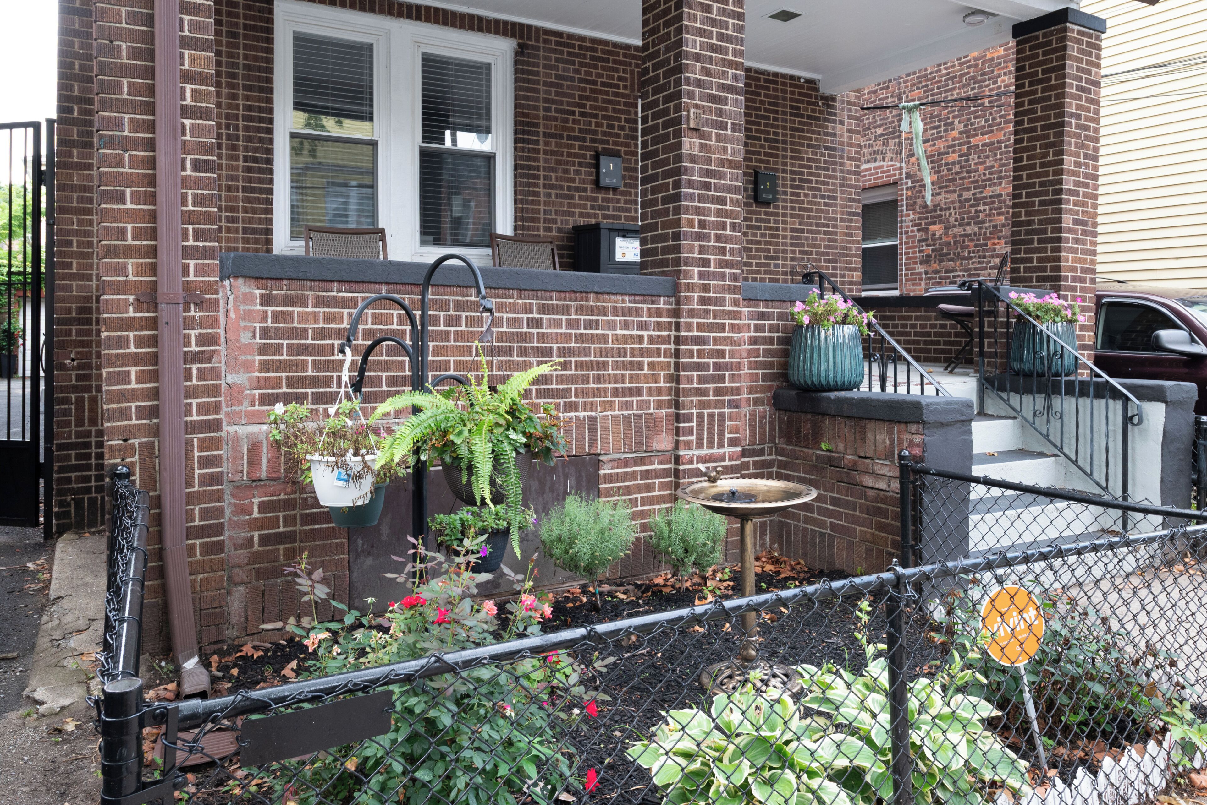 A brick house with a front porch, a small garden, and a mailbox.