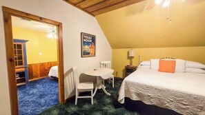 A room with a bed, a table, a chair, a poster, and a door leading to another room. - Frio Suite Gruene Cottages (New Braunfels)