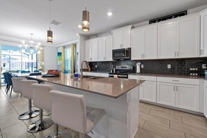 A modern kitchen with white cabinets, a central island with bar stools, a microwave, and a gas stove. - Stay in Style! 6BR Storey Lake Retreat with Pool & Spa (Kissimmee)