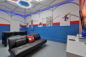 A room with a black leather couch, a foosball table, and wall art featuring Spider-Man. - Stay in Style! 6BR Storey Lake Retreat with Pool & Spa (Kissimmee)
