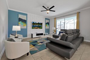 A modern living room with a sofa, a TV, and a ceiling fan. - Stay in Style! 6BR Storey Lake Retreat with Pool & Spa (Kissimmee)