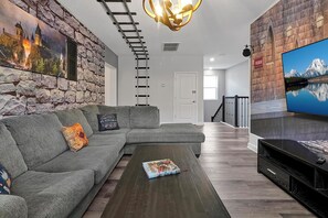 A living room with a sectional sofa, a coffee table, a mounted TV, and a stone wall with a castle mural. - Stay in Style! 6BR Storey Lake Retreat with Pool & Spa (Kissimmee)