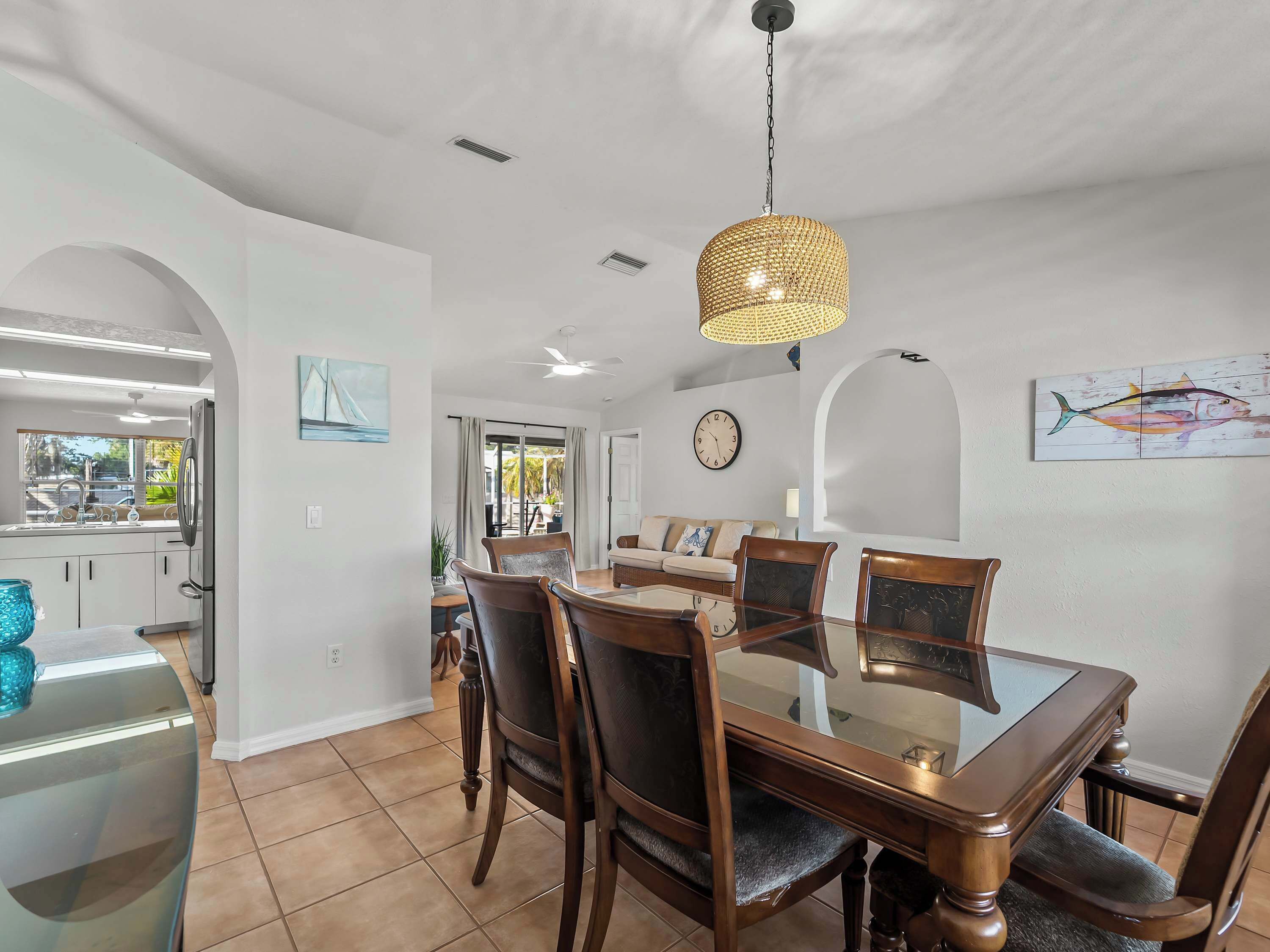A dining area with a glass-top table, wooden chairs, and a woven pendant light.
