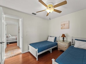 A bedroom with two beds, a ceiling fan, a bedside lamp, and a door leading to another room. - Sunlit & Spacious Solar-Heated Screened Pool, BBQ (North Port)