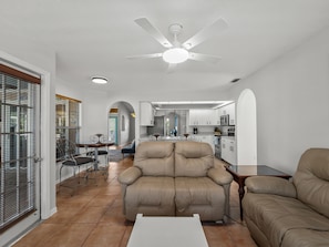 A modern living room with a beige sofa, a dining area with a table and chairs, and a kitchen in the background. - Sunlit & Spacious Solar-Heated Screened Pool, BBQ (North Port)