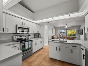 A modern kitchen with white cabinetry, a built-in oven, microwave, and a sink area. - Sunlit & Spacious Solar-Heated Screened Pool, BBQ (North Port)