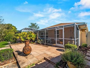 Ein Haus mit überdachter Terrasse, einer großen Pflanze im Topf und einem Garten.