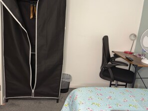 Un dormitorio con cama, escritorio, silla, armario y un cubo de basura.