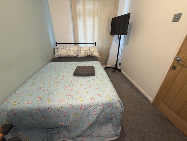 Una habitación pequeña y estrecha con una cama, un televisor de pantalla plana en la pared y una puerta.