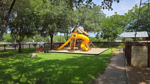 Ein Spielplatz mit Rutsche und Klettergerüst, umgeben von Bäumen und einem Zaun.