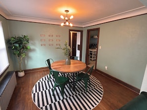 A dining area with a round wooden table, green chairs, a black and white striped rug, a potted plant, and a ceiling light fixture. - Paws on Lowry: Mint Sleek Retro • Pet-Friendly (Minneapolis)