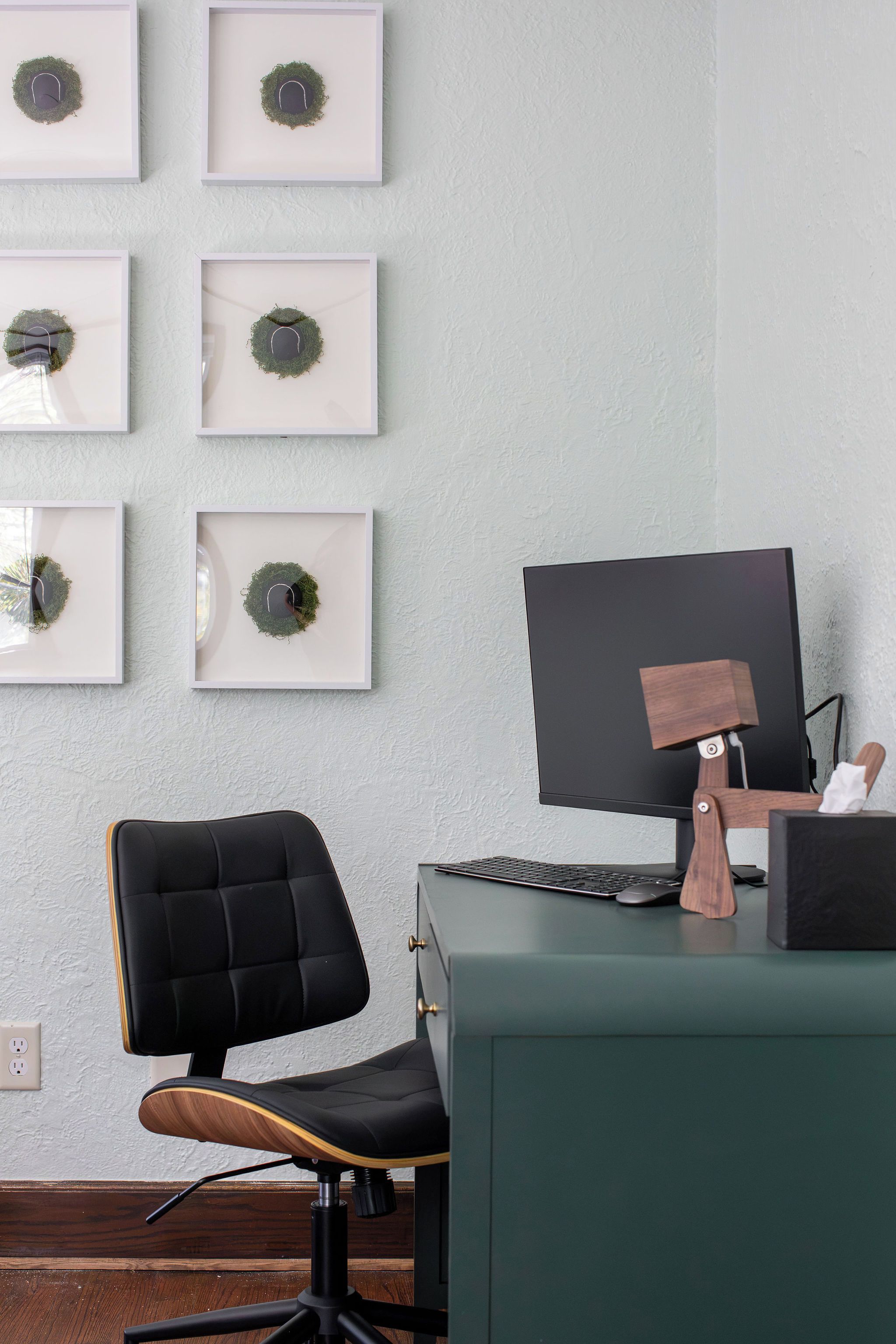 A workspace with a desk, computer, chair, and framed wall decorations.