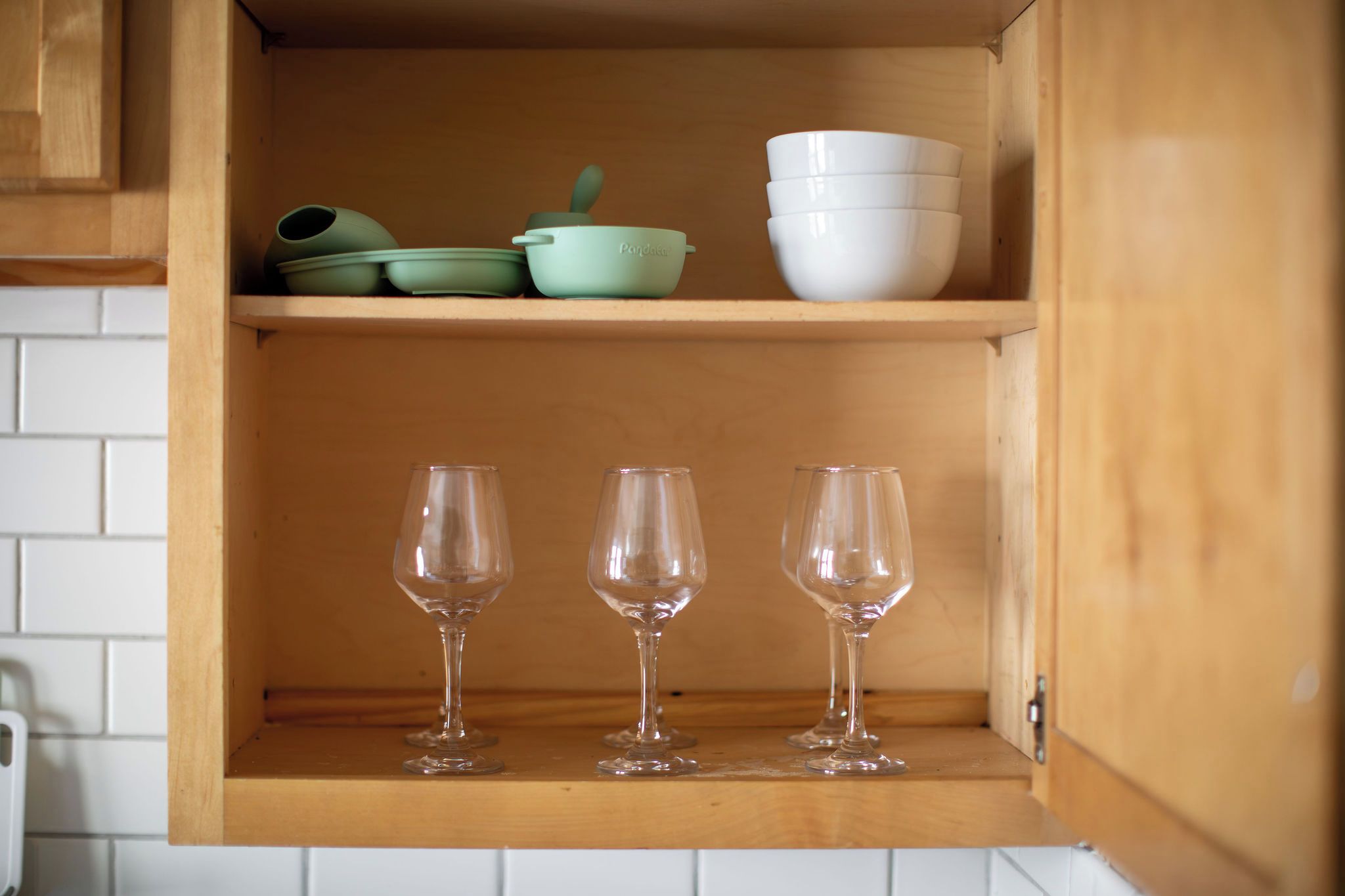 A wooden cabinet with three wine glasses and various bowls.
