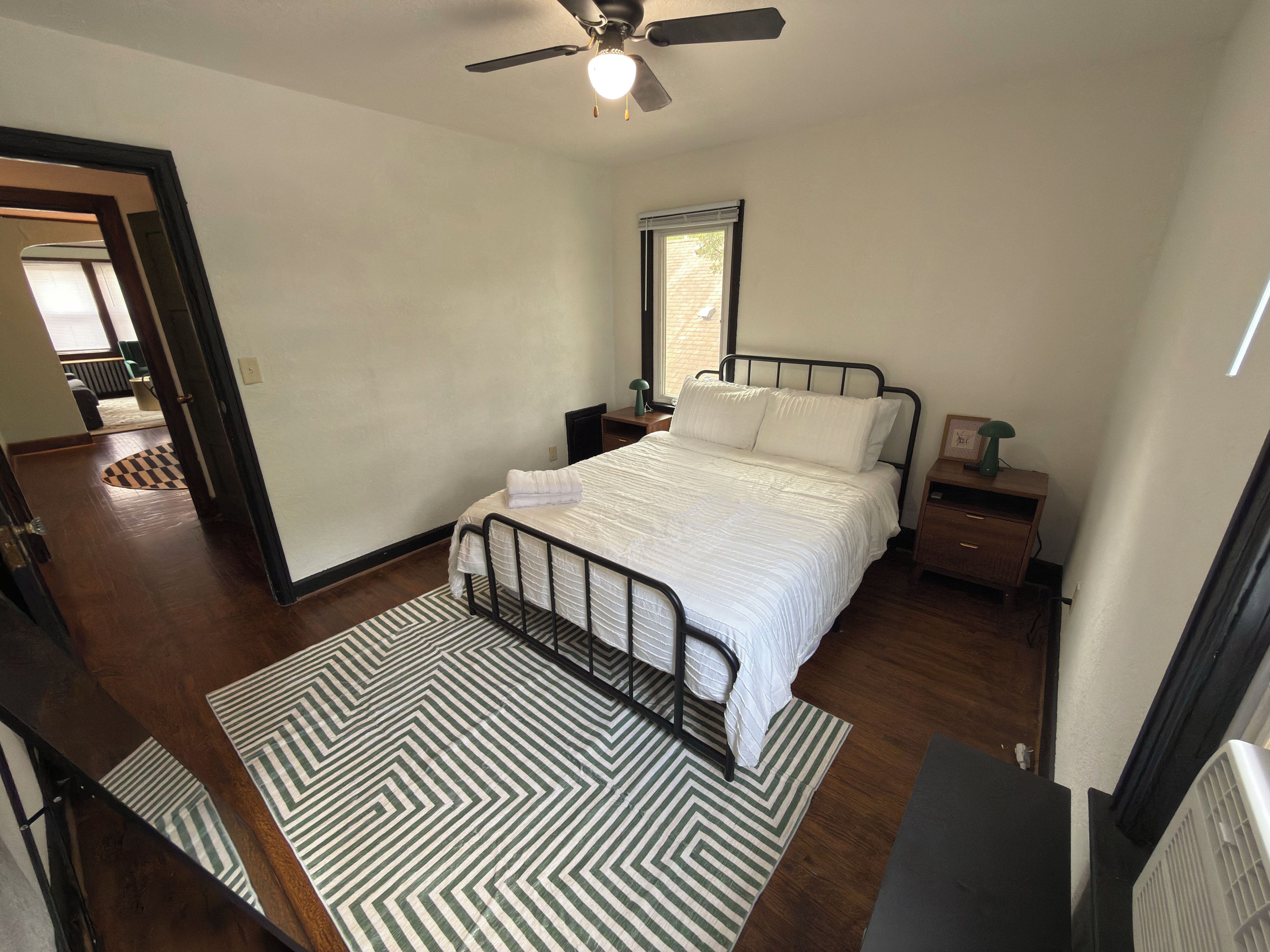 A bedroom with a bed, bedside tables, a ceiling fan, a window, and a patterned rug.