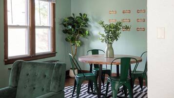 Un comedor con mesa de madera, sillas verdes, una planta en maceta y un tapete de cuadros blancos y negros.