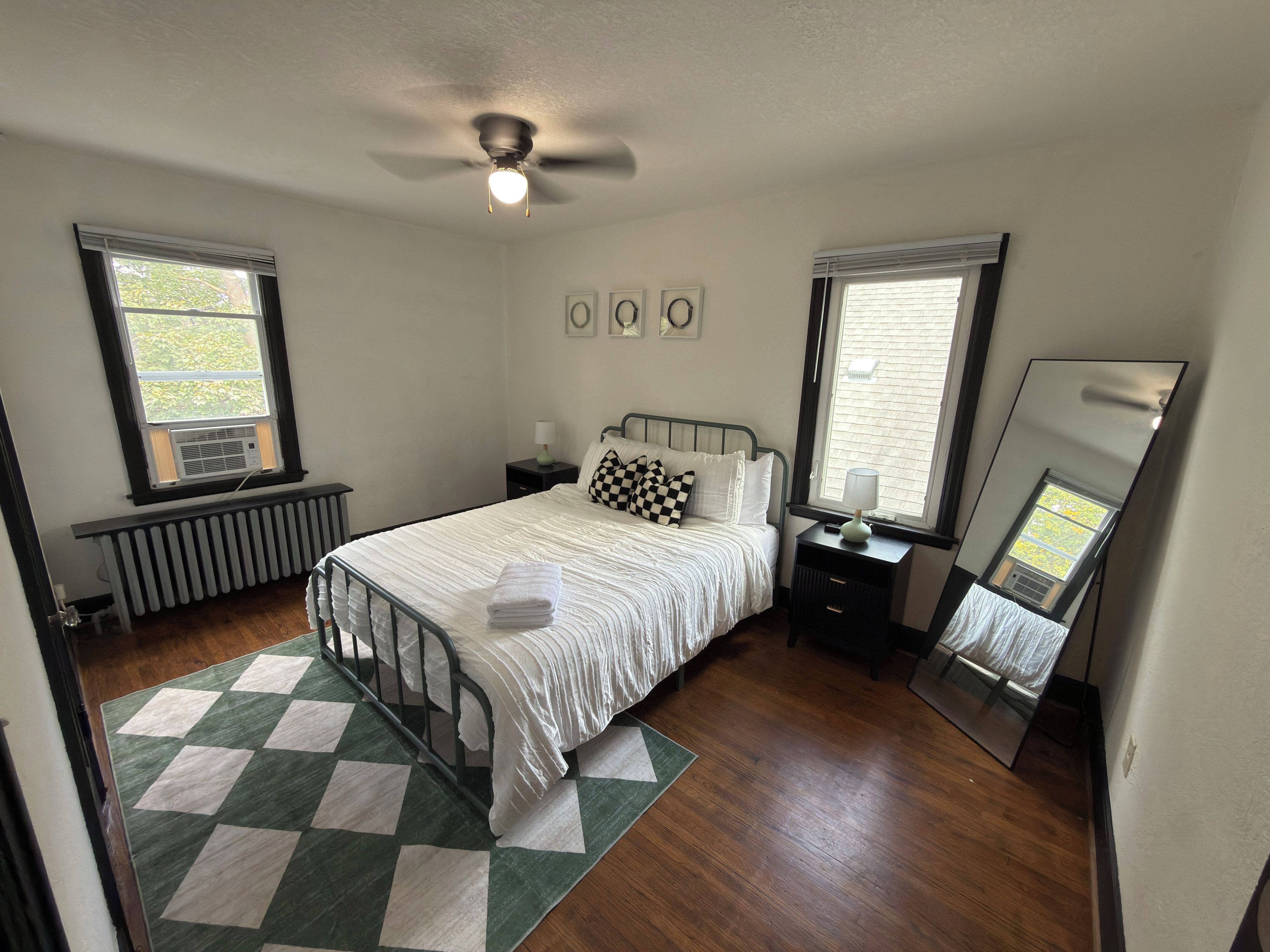 A bedroom with a bed, a radiator, a window, a ceiling fan, and a mirror.