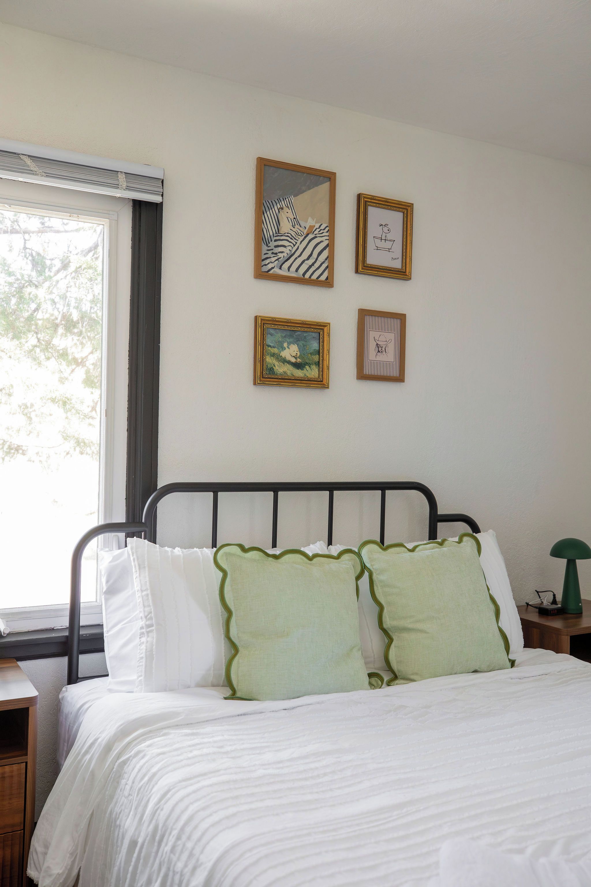 Um quarto com cama, janela e quatro obras de arte emolduradas na parede.