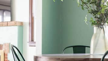 A dining area with a wooden table and green chairs, a striped rug, and a potted plant.