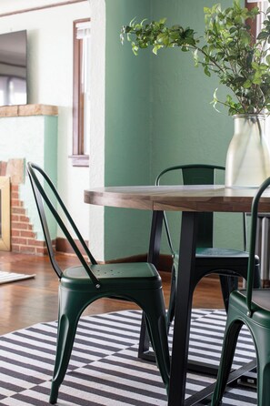 Un comedor con una mesa de madera y sillas verdes, un tapete a rayas y una planta en maceta.