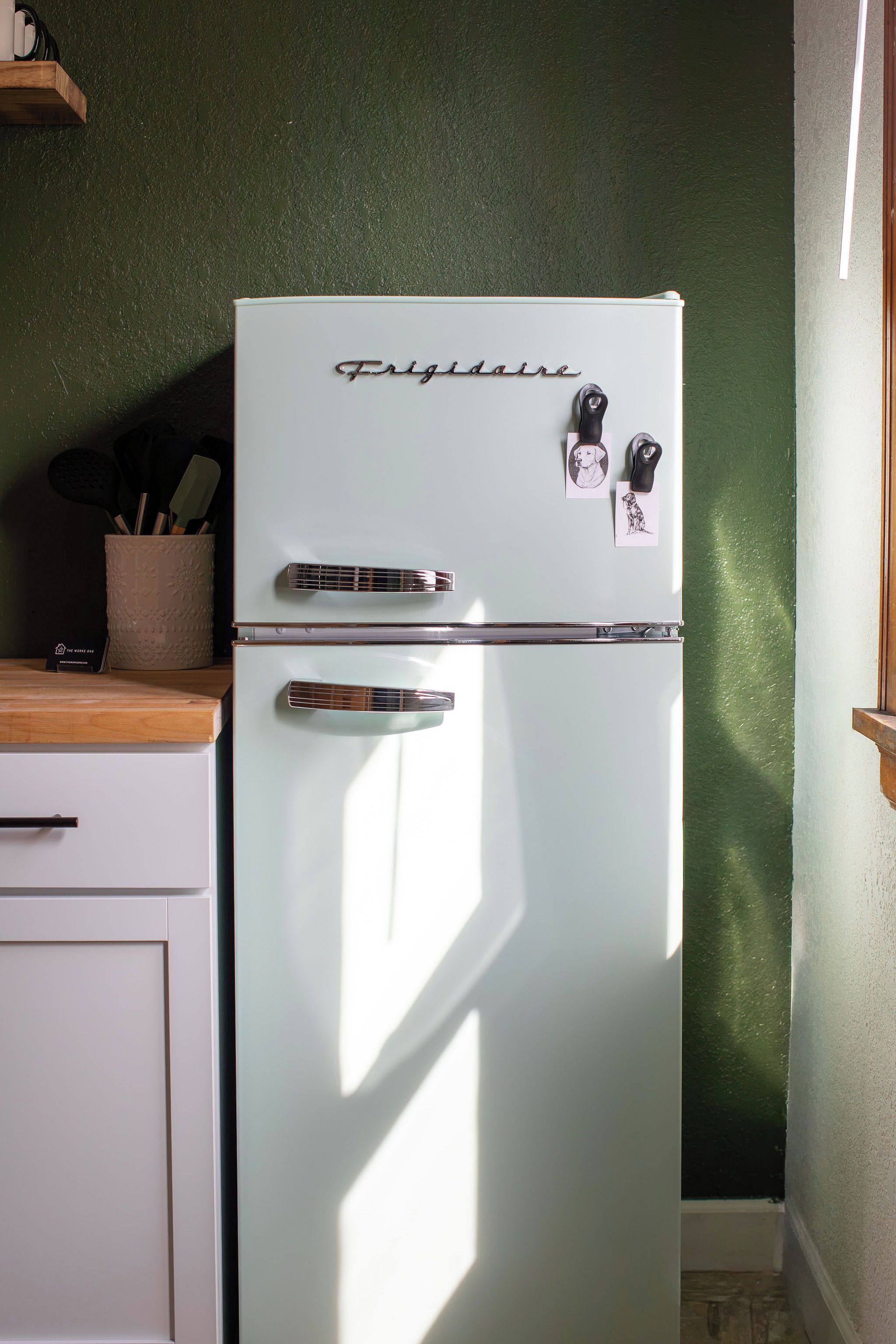 A white Frigidaire refrigerator with a chrome handle and two key holders, against a green wall.