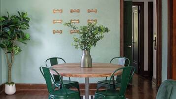 Un espace repas avec une table ronde en bois, des chaises vertes, une plante en pot et des panneaux fixés au mur indiquant différents parcs.