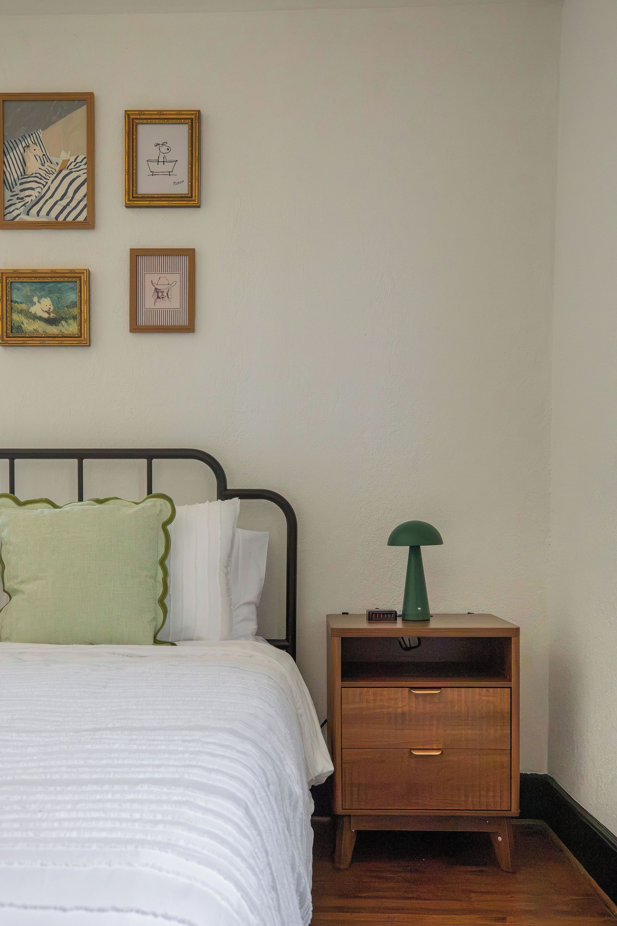 A bedroom with a bed, a nightstand, and a wall with framed artwork.