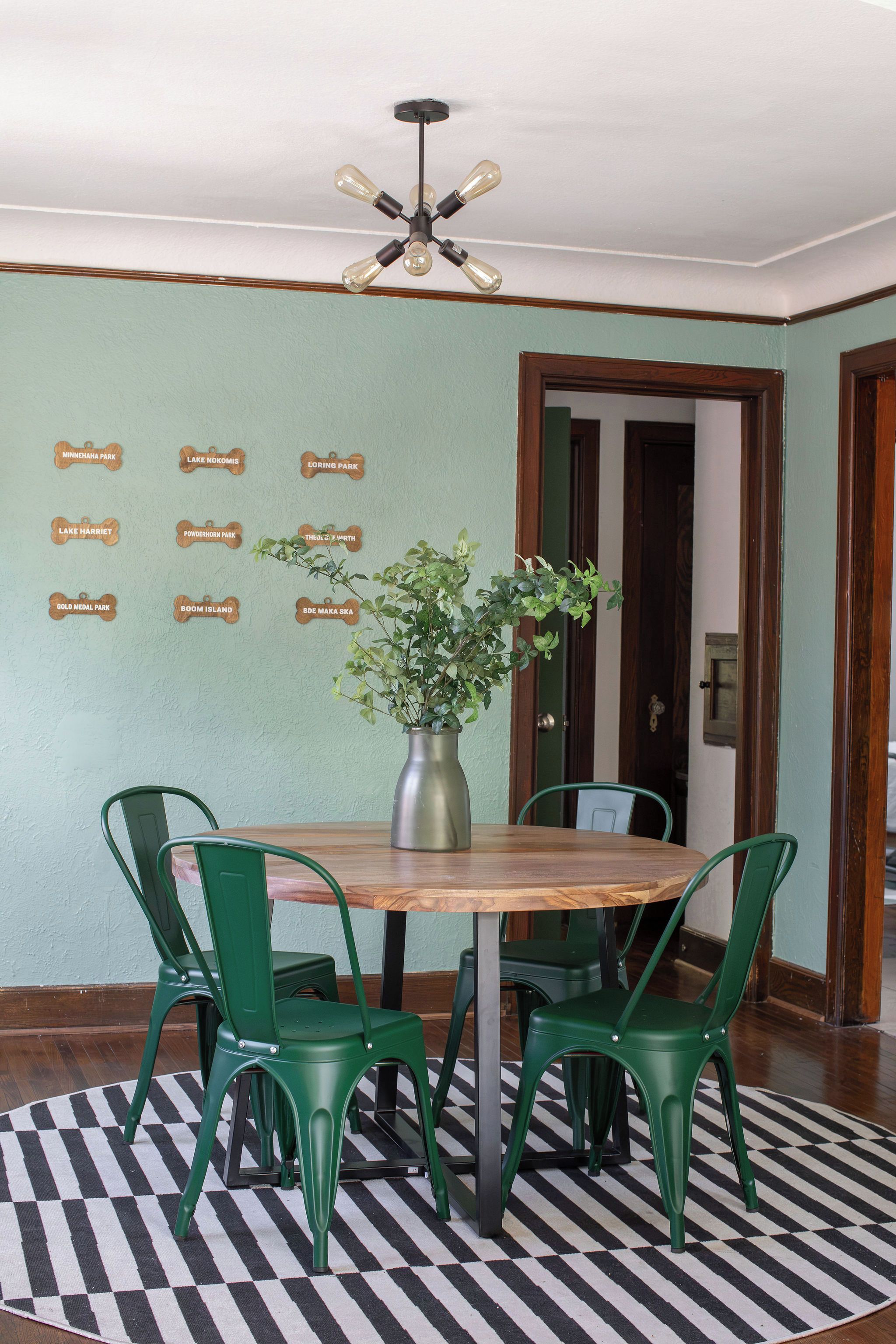 A dining area with a wooden table, green chairs, a potted plant, and a wall with park name plaques.