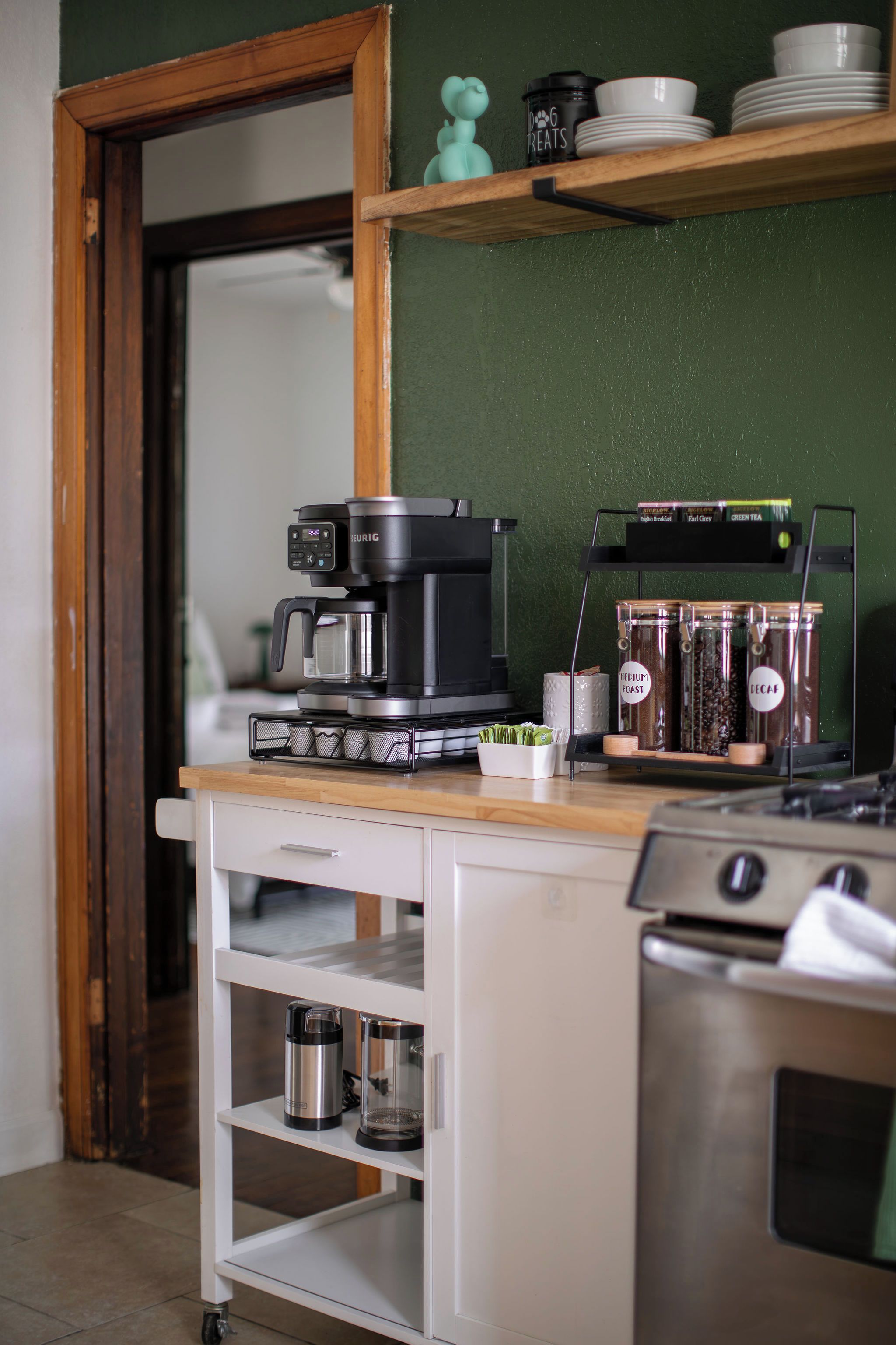 Une petite cuisine équipée d’une machine à café, de pots de thé et d’un récipient contenant des friandises pour chiens.