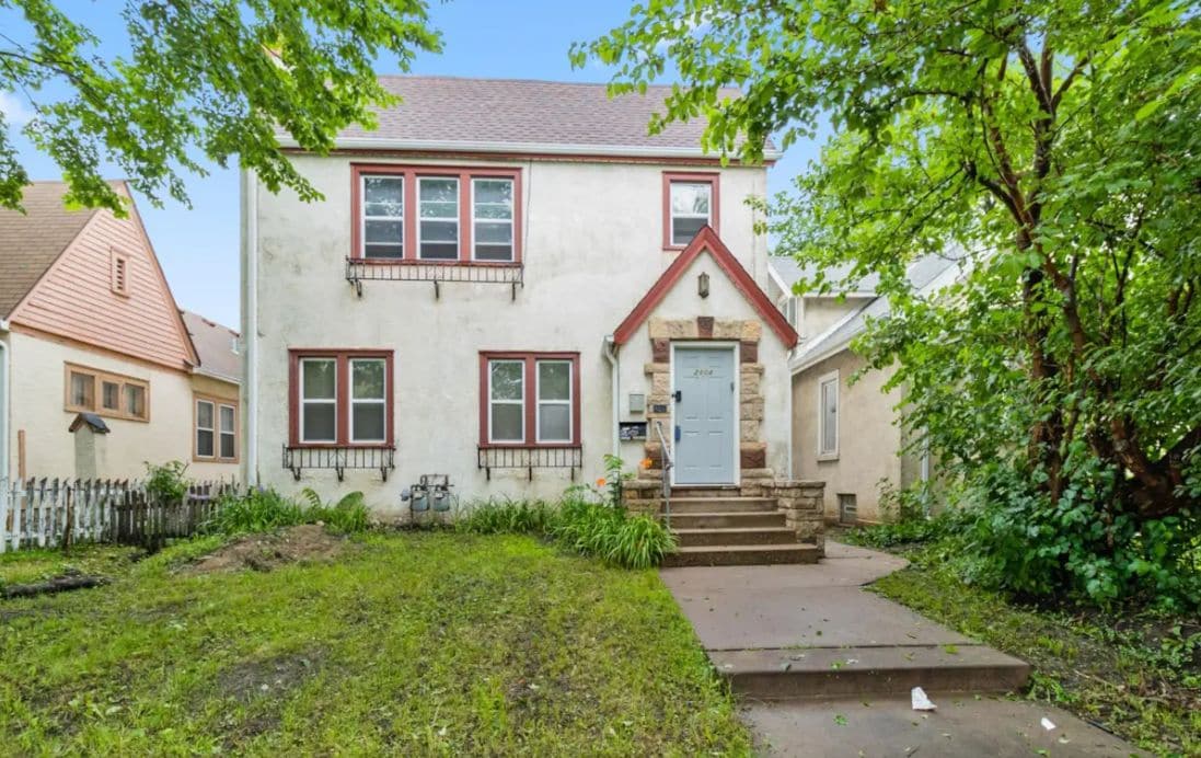 A two-story house with a front porch, a stone foundation, and a red roof.