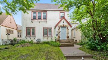 A two-story house with a front porch, a stone foundation, and a red roof.